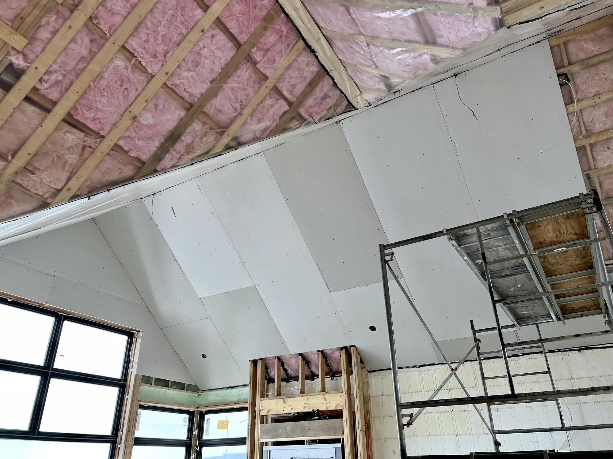 A vaulted ceiling half boarded with gypsum over pink batt insulation, scaffold in position